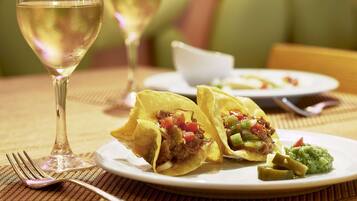 Una mesa de comedor con un plato de tacos, una copa de vino blanco y un tenedor.