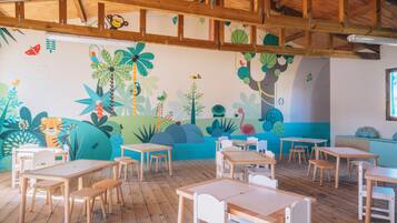 A classroom with wooden tables and chairs, a mural with tropical and animal designs, and a wooden ceiling structure.
