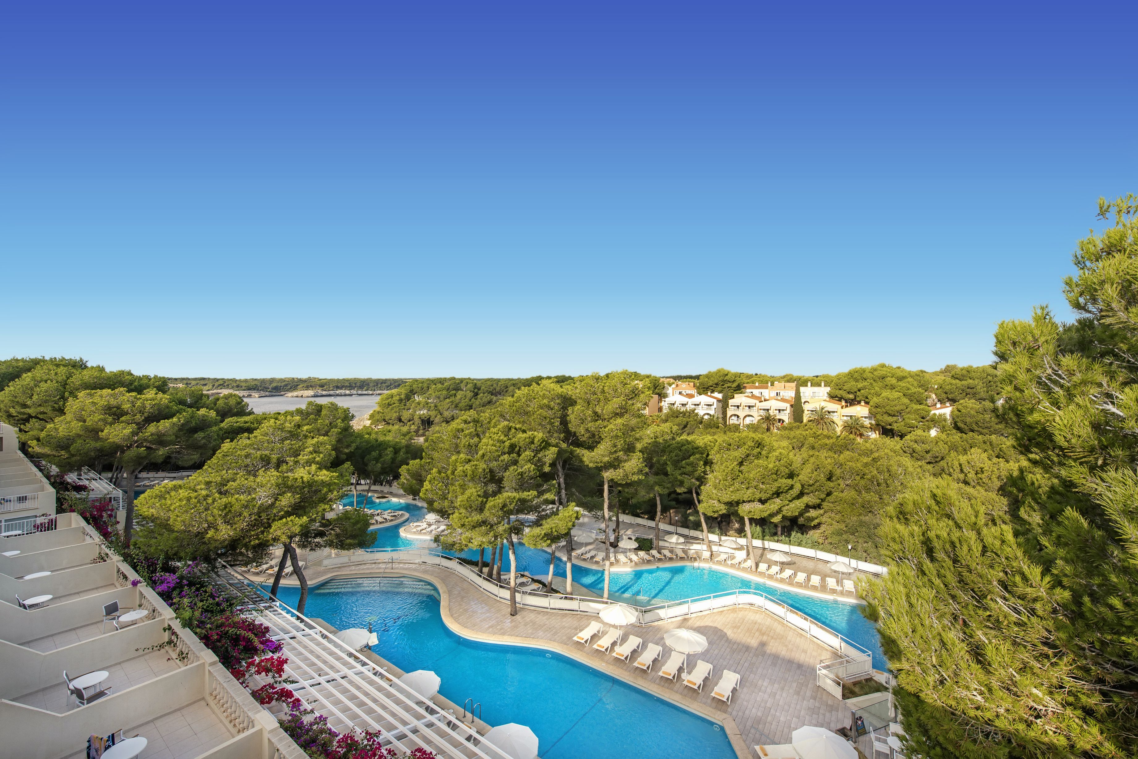 Zona de piscina en un resort con varias piscinas, sillas de descanso y vistas del paisaje circundante.