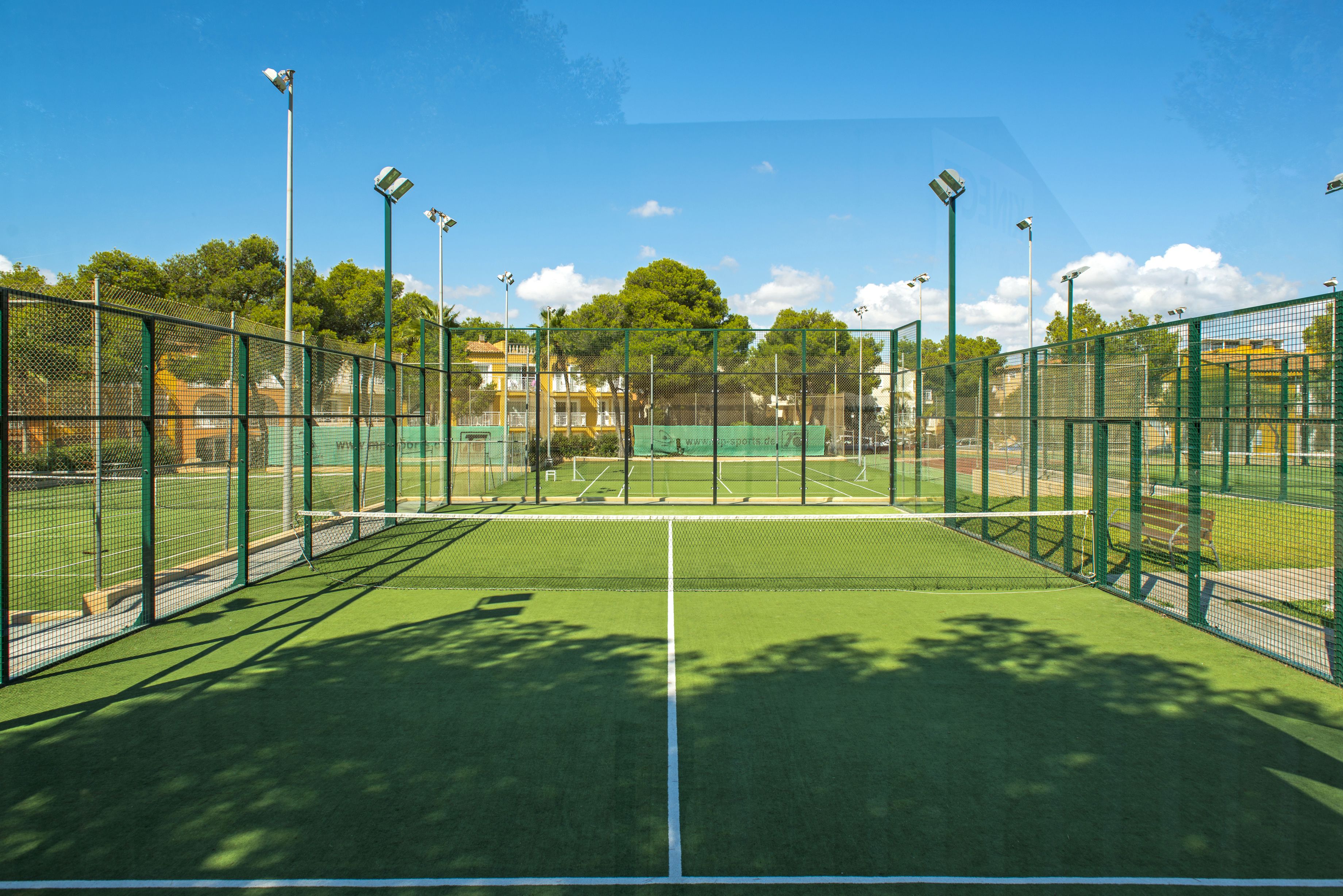 Ein Tennisplatz mit Netz, umgeben von einem grünen Zaun und Bäumen im Hintergrund.