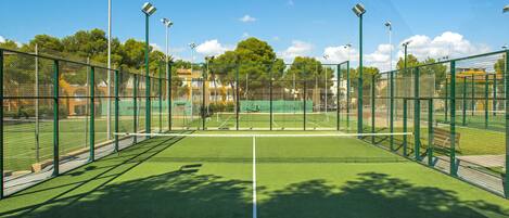 Ein Tennisplatz mit Netz, umgeben von einem grünen Zaun und Bäumen im Hintergrund.