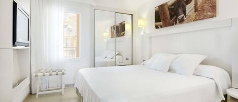 A hotel room with a large bed, a TV, a bedside table, a mirror, and a window with curtains.