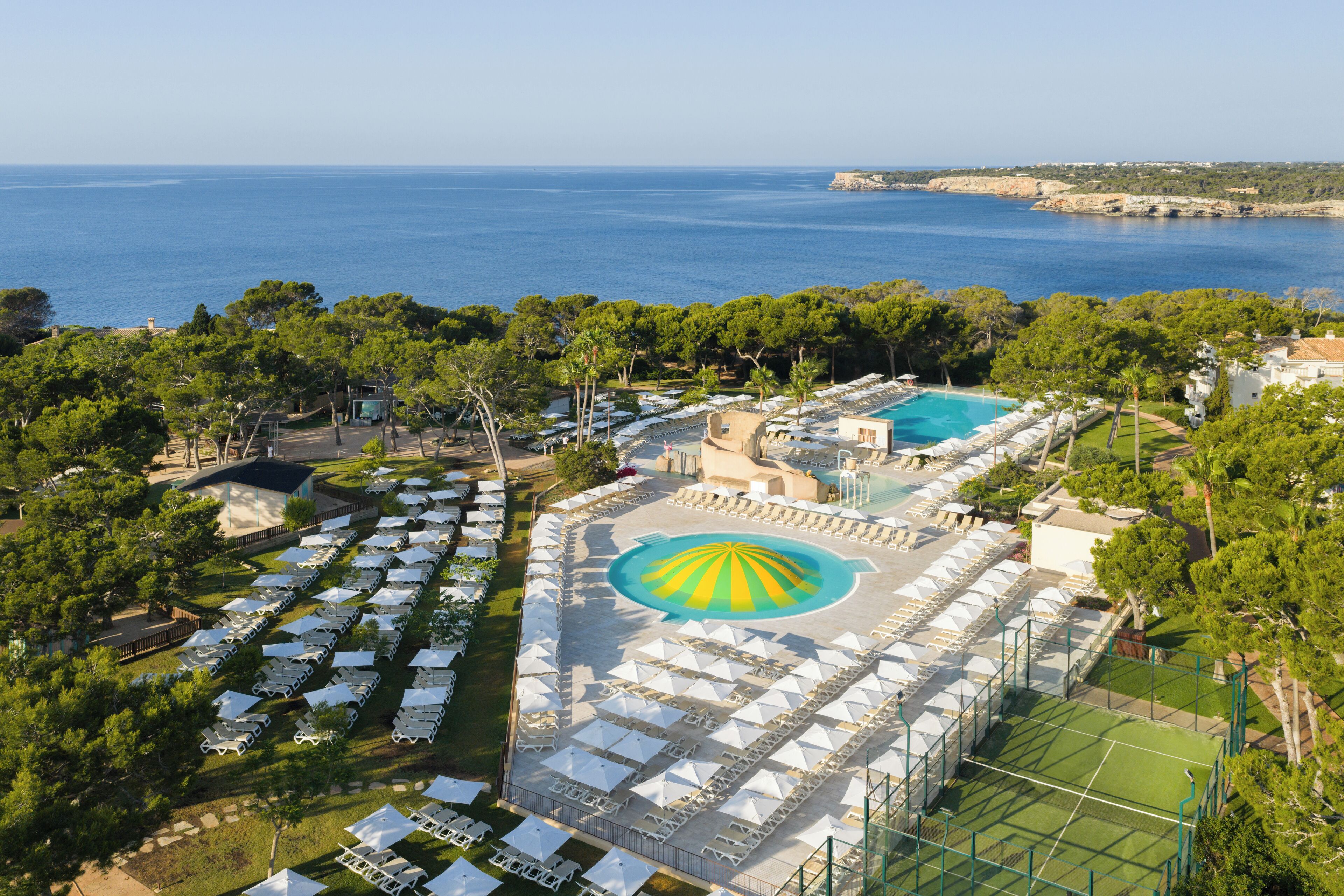Vista aérea de un resort con múltiples piscinas, sillas de descanso y una gran piscina central con un diseño distintivo.