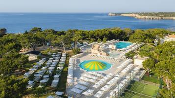 Vista aérea de un resort con múltiples piscinas, sillas de descanso y una gran piscina central con un diseño distintivo.