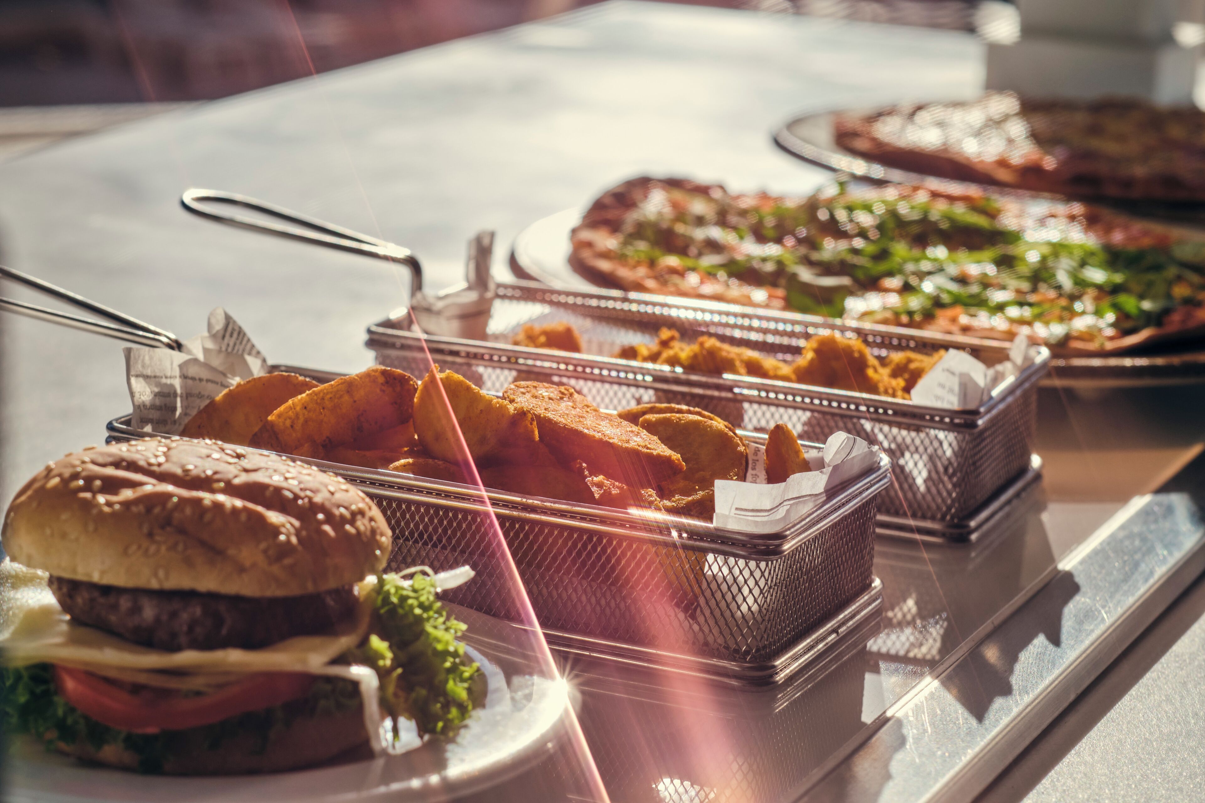 A buffet table with various food items including burgers, fries, and pizzas.