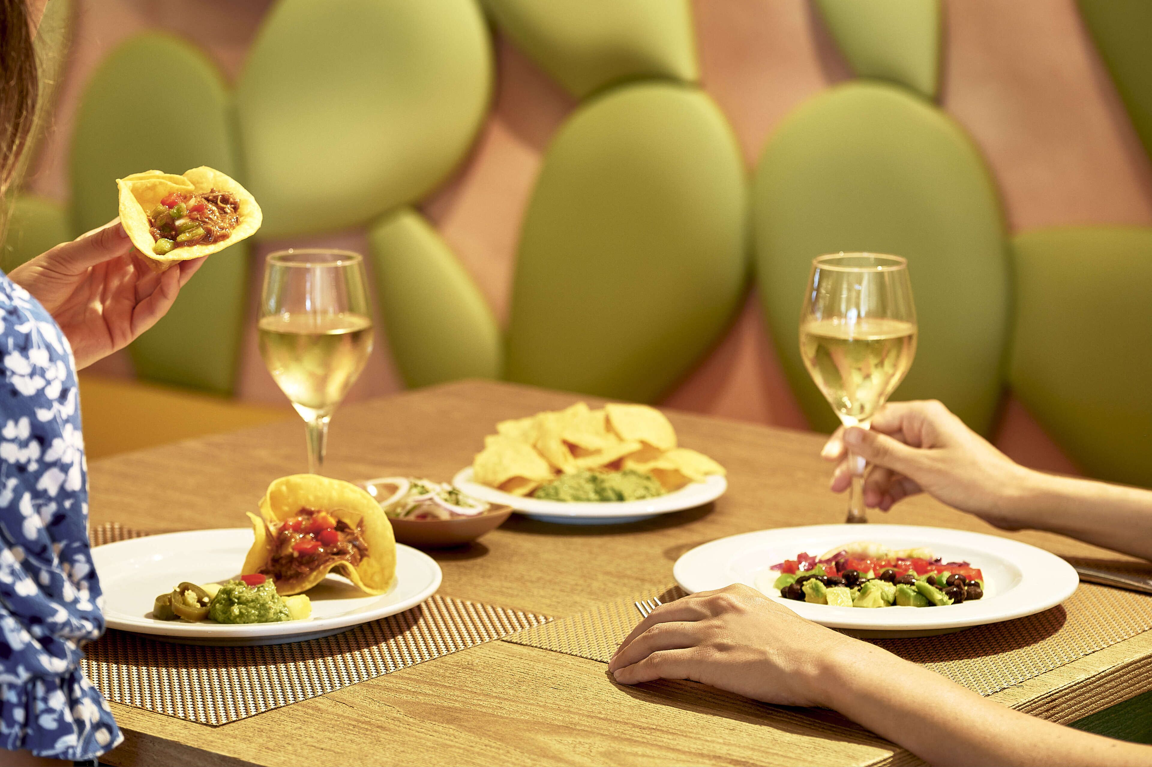 Une table à manger avec des assiettes remplies de nourriture, notamment des tacos et une salade, ainsi que deux verres de vin.