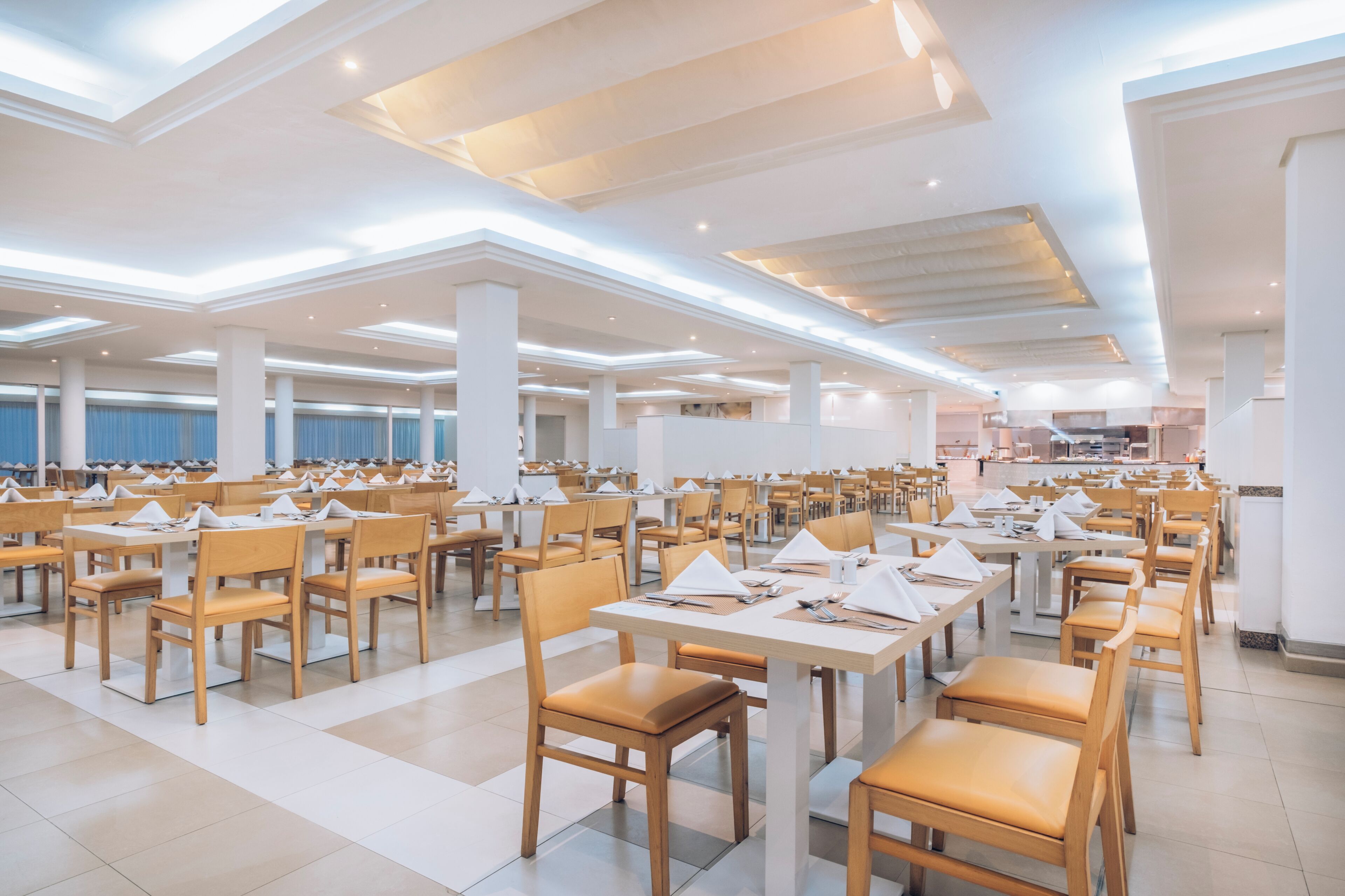 A spacious dining area with multiple tables and chairs, high ceilings with recessed lighting, and a modern architectural design.