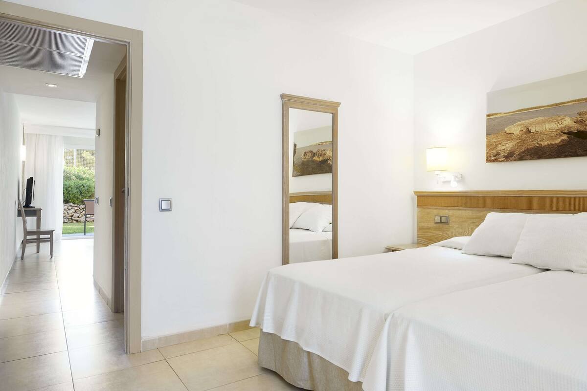 A hotel room with a bed, a bedside table, a mirror, and a painting on the wall.