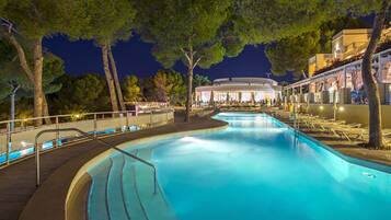 Ein Pool mit geschwungener Form, umgeben von Bäumen und einem Gebäude mit einer runden Struktur im Hintergrund.