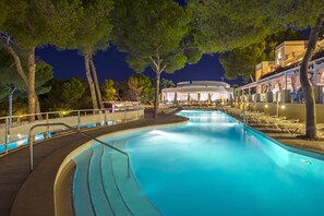 A swimming pool with a curved design, surrounded by trees and a building with a circular structure in the background.