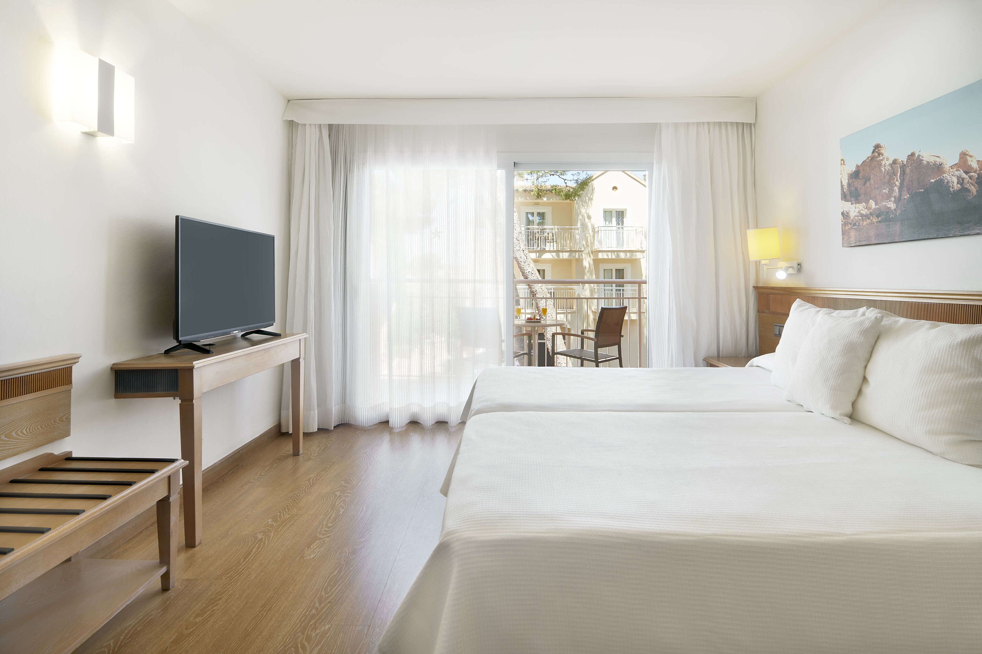 Une chambre d’hôtel avec un lit, un bureau avec une télévision, une chaise et une fenêtre avec des rideaux.