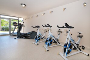 Une salle de sport équipée de vélos d’appartement, d’un tapis de course et d’une grande fenêtre donnant sur un paysage verdoyant.
