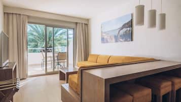 Una habitación de hotel moderna con una mesa de comedor de madera, un sofá y vistas a palmeras a través del ventanal.