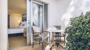 Una habitación de hotel moderna con puerta corrediza de vidrio que da a un balcón, una pequeña mesa con una silla y una planta en maceta.