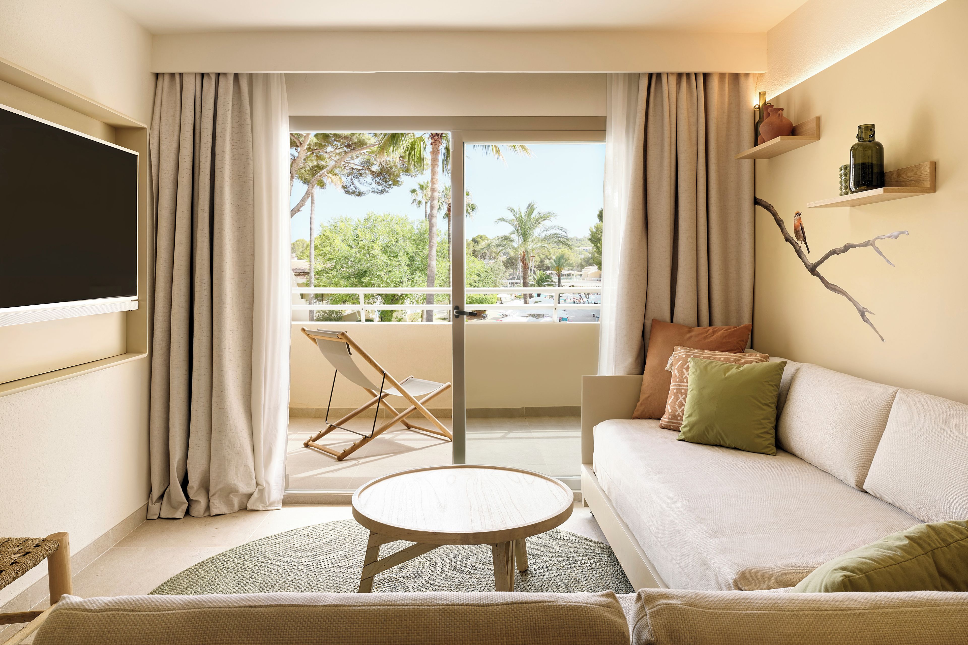 A modern living room with a sofa, a small round table, and a view of a balcony with a chair.