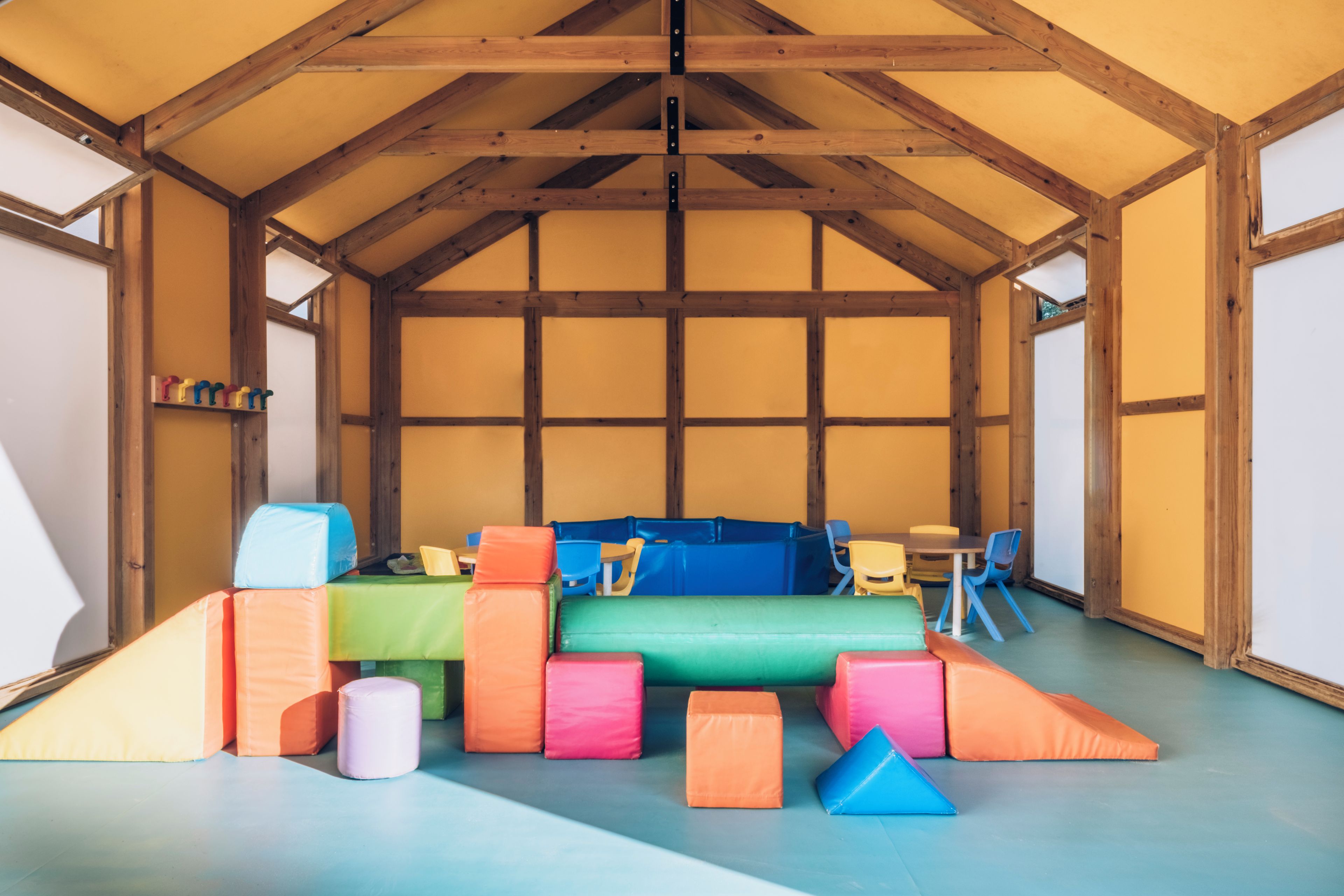 A room with a high ceiling and wooden beams, featuring colorful padded seating and tables.