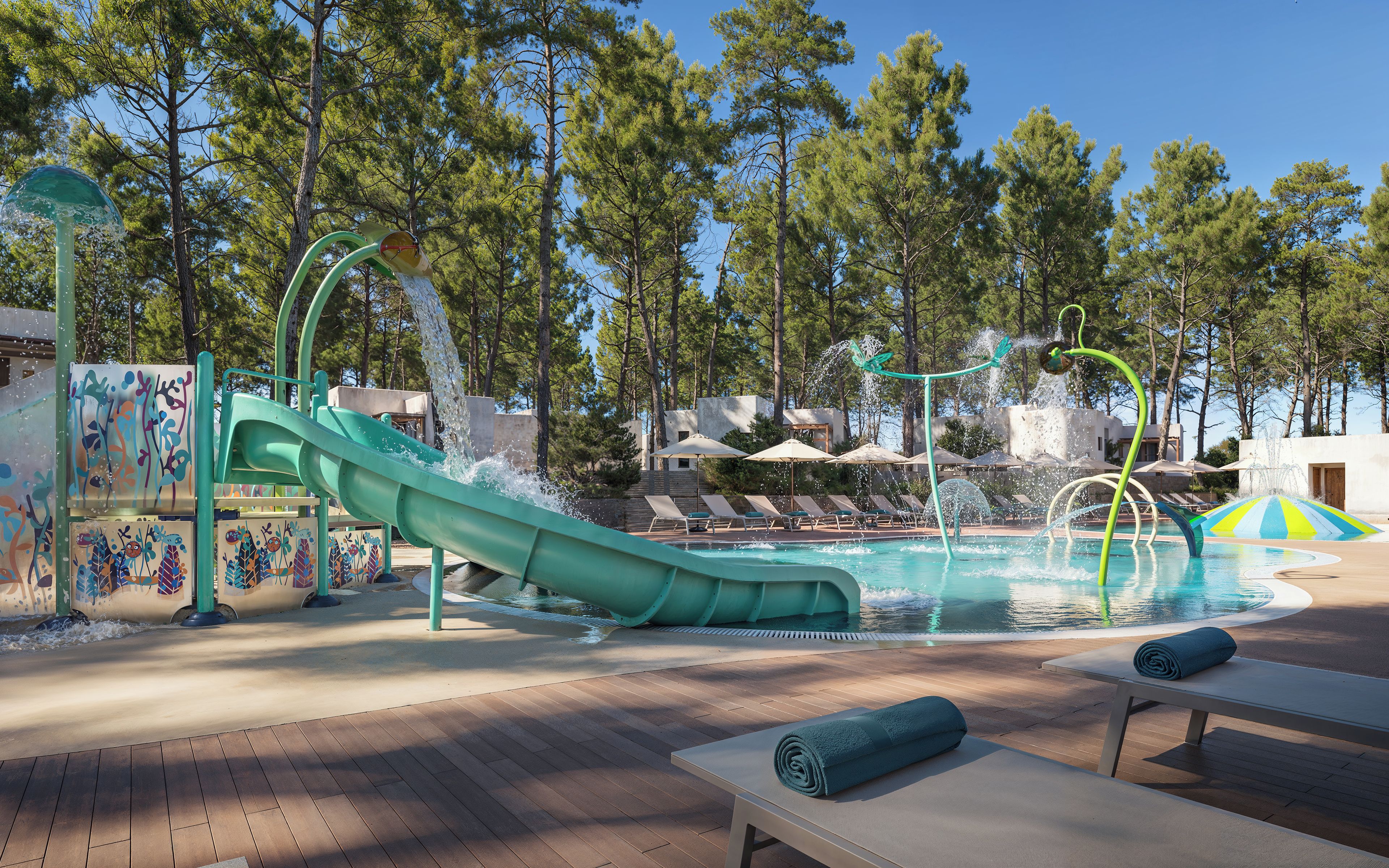 A pool area with a water slide, lounge chairs, and umbrellas.