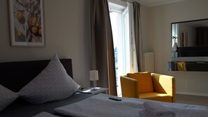 A hotel room with a bed, a chair, a desk, a lamp, and a window with curtains. - Hotel Milano (Hildesheim)