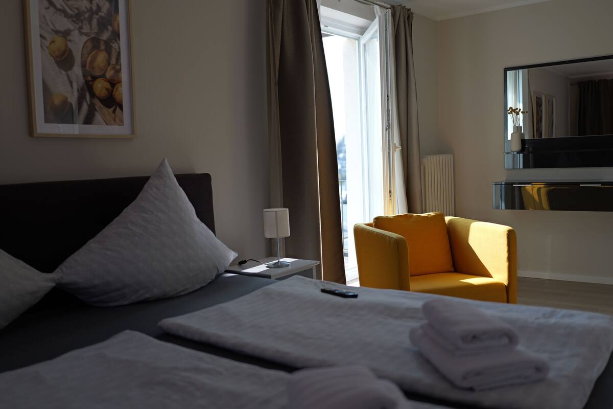 A hotel room with a bed, a chair, a desk, a lamp, and a window with curtains.