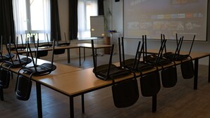 A conference room with long tables, chairs, a projector screen, and a whiteboard. - Hotel Milano (Hildesheim)