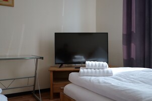 Una habitación de hotel con una cama, un televisor sobre un mueble de madera y una estantería de vidrio.