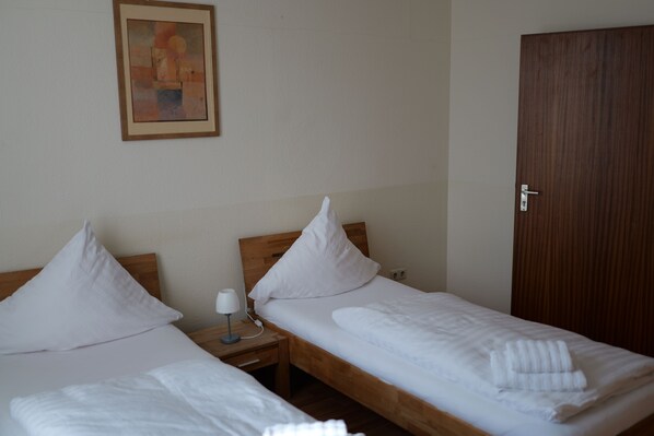 Two single beds with wooden frames and white bedding, a nightstand with a lamp, and a wooden door. - Hotel Milano (Hildesheim)