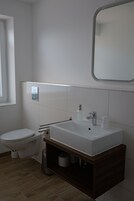 Un baño moderno con lavamanos, espejo y retrete blancos.