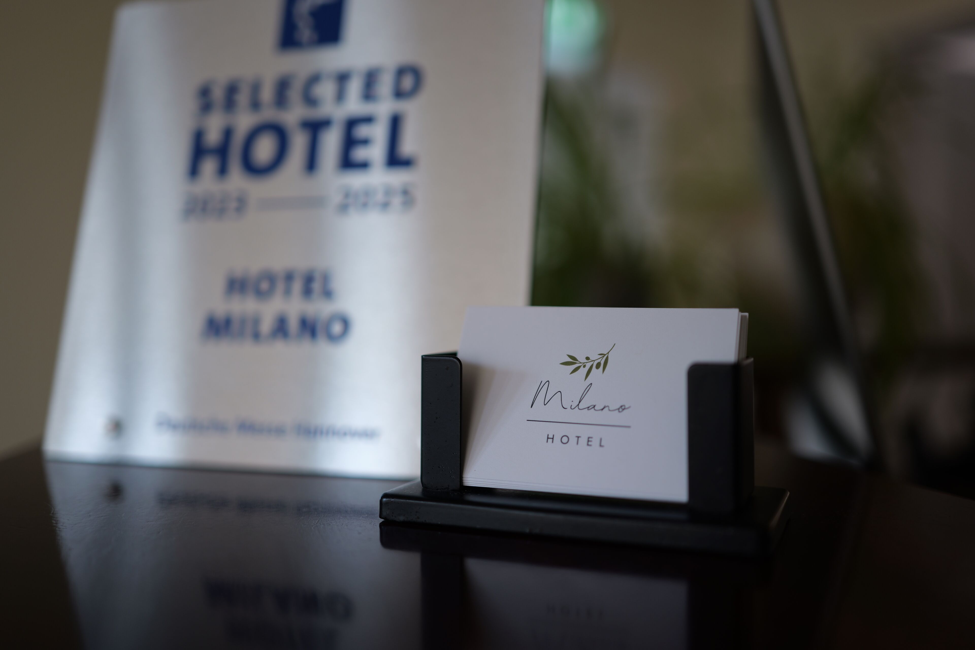 A hotel name card for Milano Hotel with a black stand.