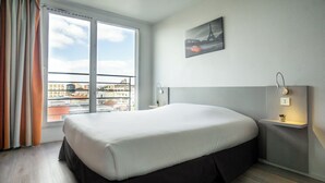 A modern hotel room with a large bed, a view of the city through a balcony, and a painting of the Eiffel Tower. - City Residence Ivry (Ivry-sur-Seine)