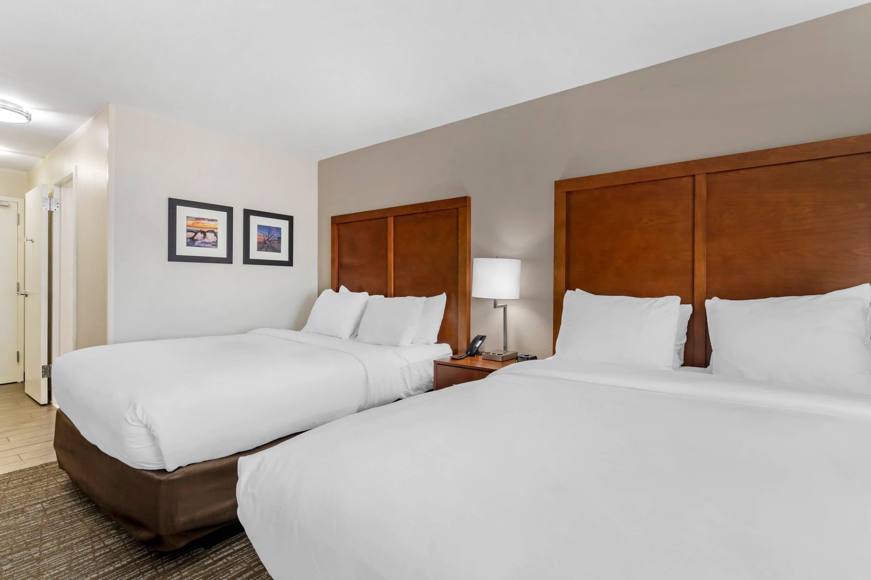 A hotel room with two single beds, a wooden headboard, a bedside table with a lamp, and two framed pictures on the wall.
