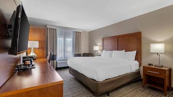 A hotel room with a large bed, a desk with a telephone, a television, and a window with curtains.