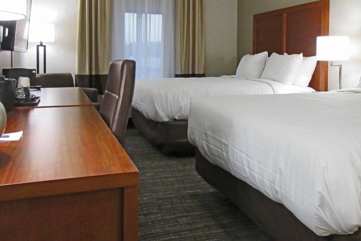 A hotel room with two beds, a wooden desk, a chair, and a lamp.