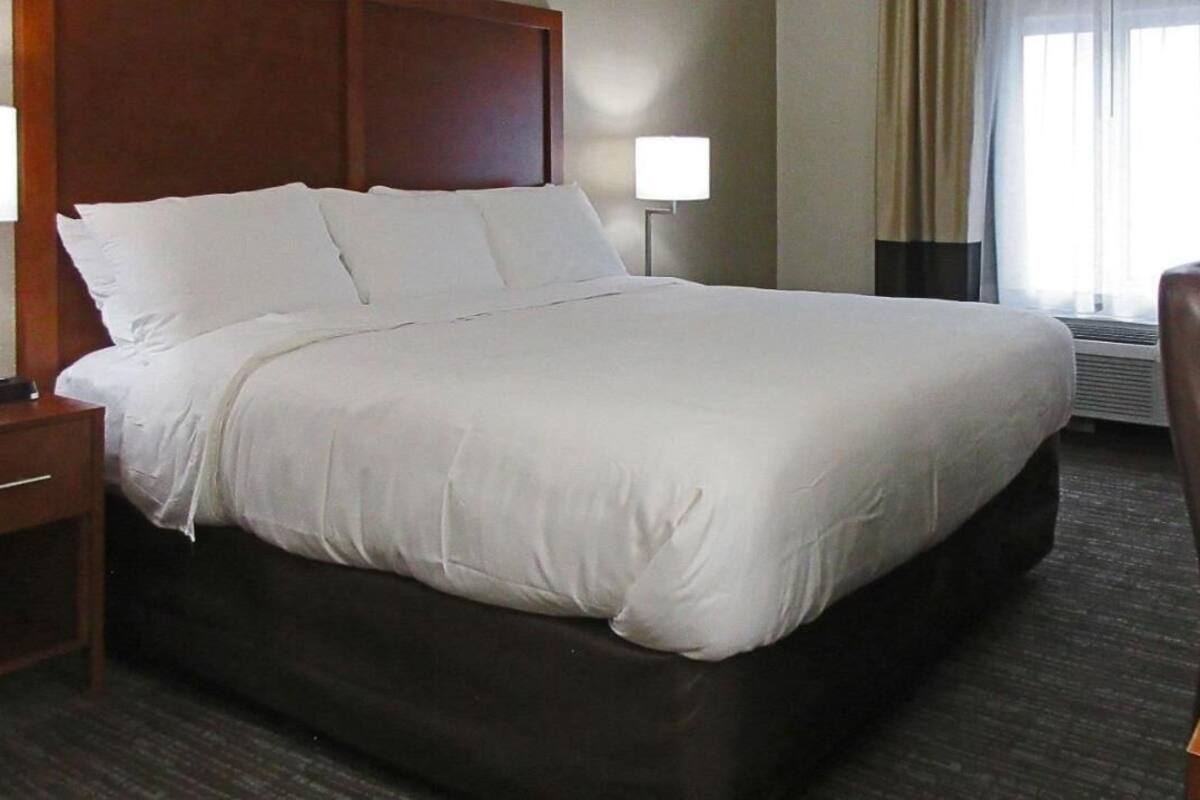 A hotel room with a large bed, a bedside table, a lamp, a chair, and a window with curtains.