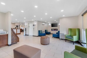 A hotel lobby with a reception desk, seating area, and a staircase.