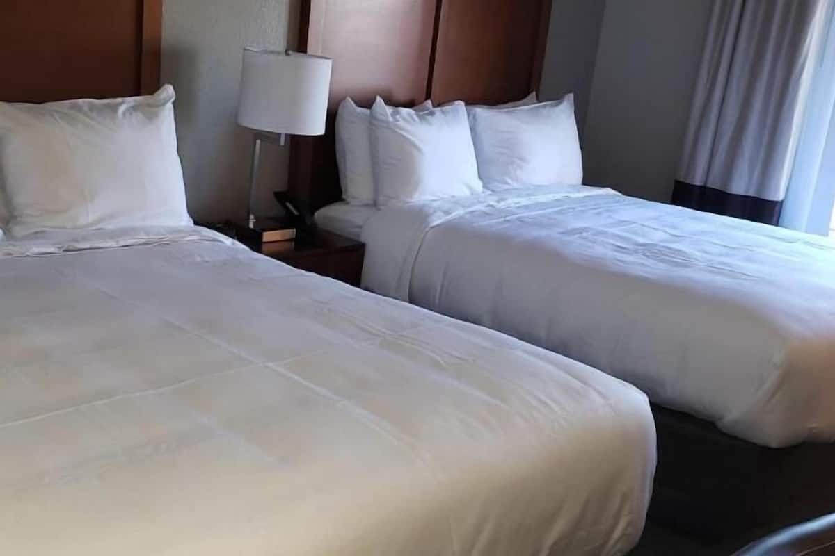 Two beds with white linens, a bedside lamp, and a wooden headboard.