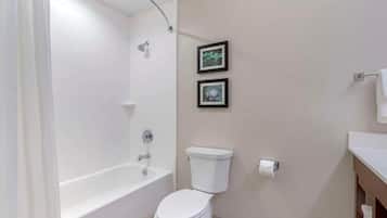 A bathroom with a bathtub, toilet, and two framed pictures on the wall.