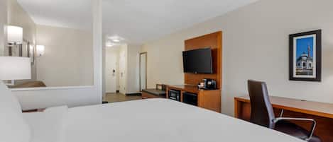 Habitación de hotel con cama, escritorio, silla, televisor y un cuadro en la pared.
