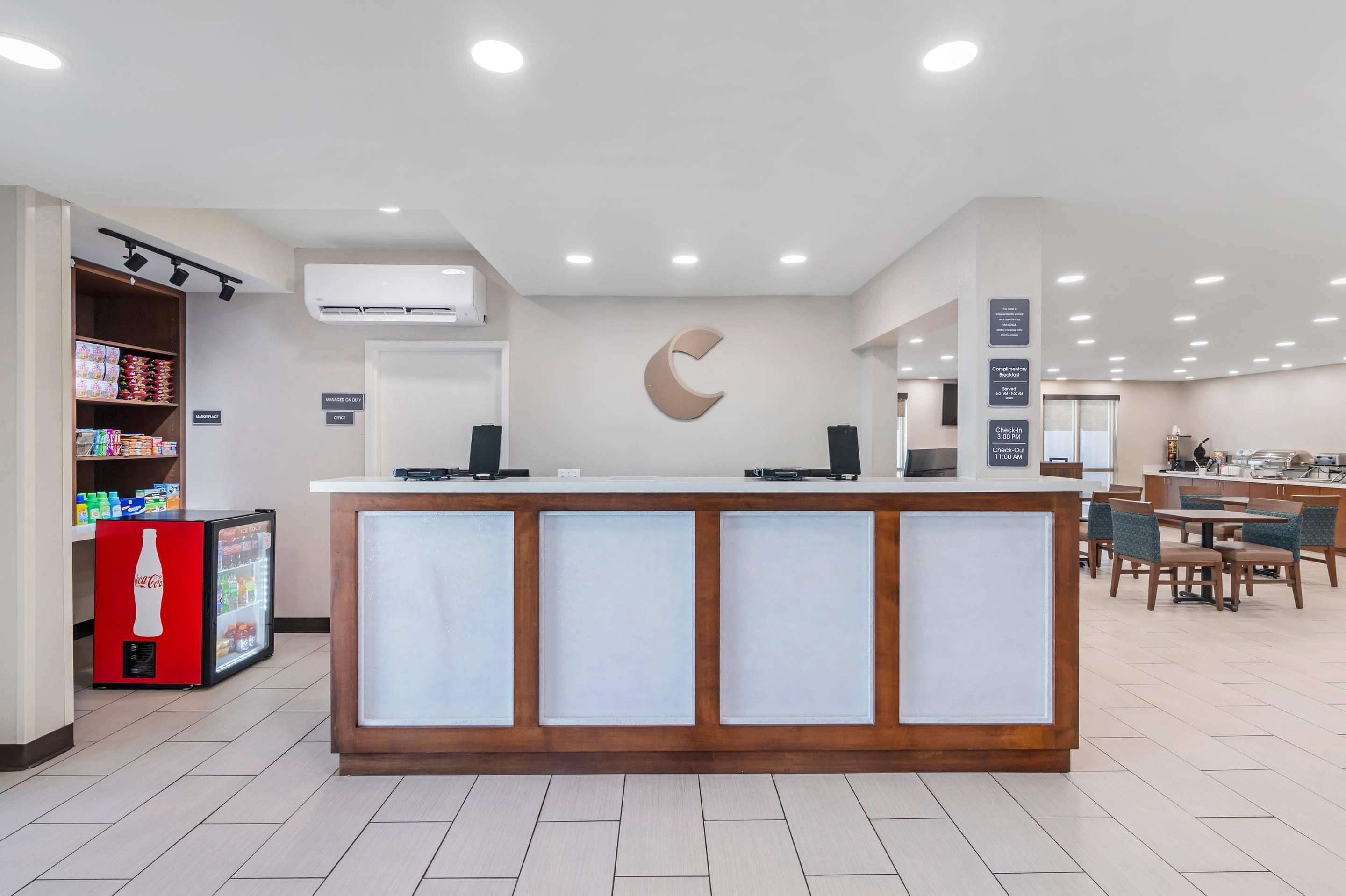A hotel reception area with a counter, a refrigerator, and a seating area with tables and chairs.