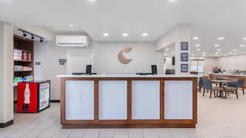 A hotel reception area with a counter, a refrigerator, and a seating area with tables and chairs.