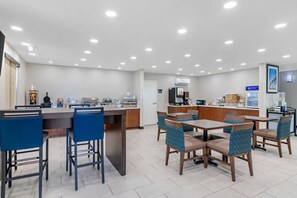 A modern hotel dining area with a bar, seating, and a kitchen in the background.