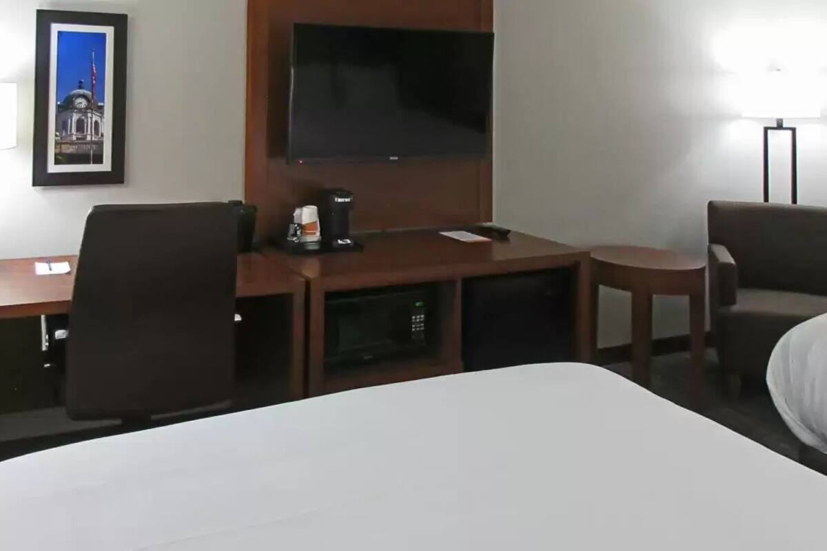 A hotel room with a large bed, a desk with a chair, a television, and a lamp.