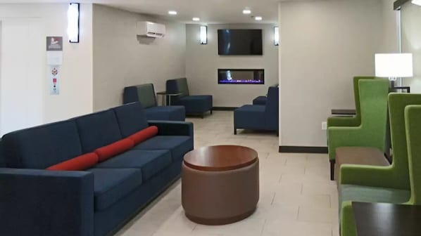 A modern lobby with blue and green seating, a flat-screen TV, and a fireplace.