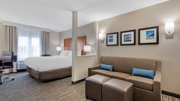Habitación de hotel con una cama grande, un sofá, una mesita y una silla. Hay dos lámparas de pared y tres cuadros enmarcados.