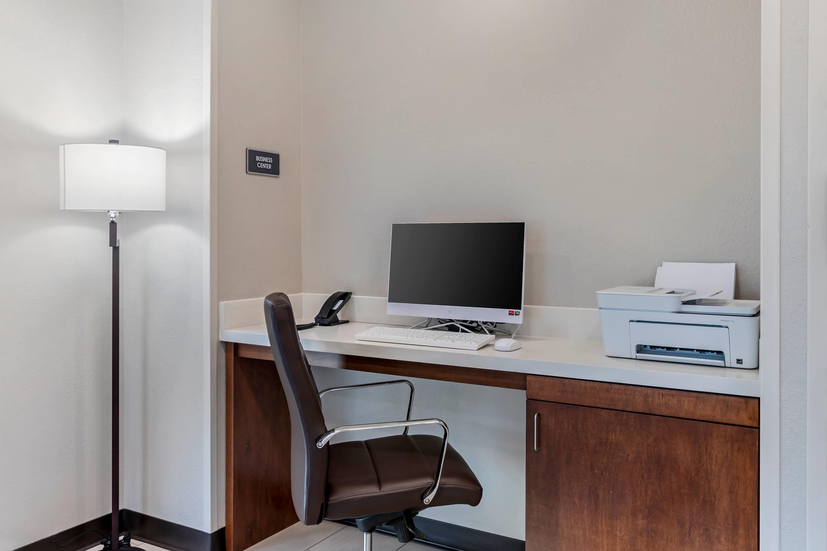 A hotel business center with a desk, computer, printer, and a chair.