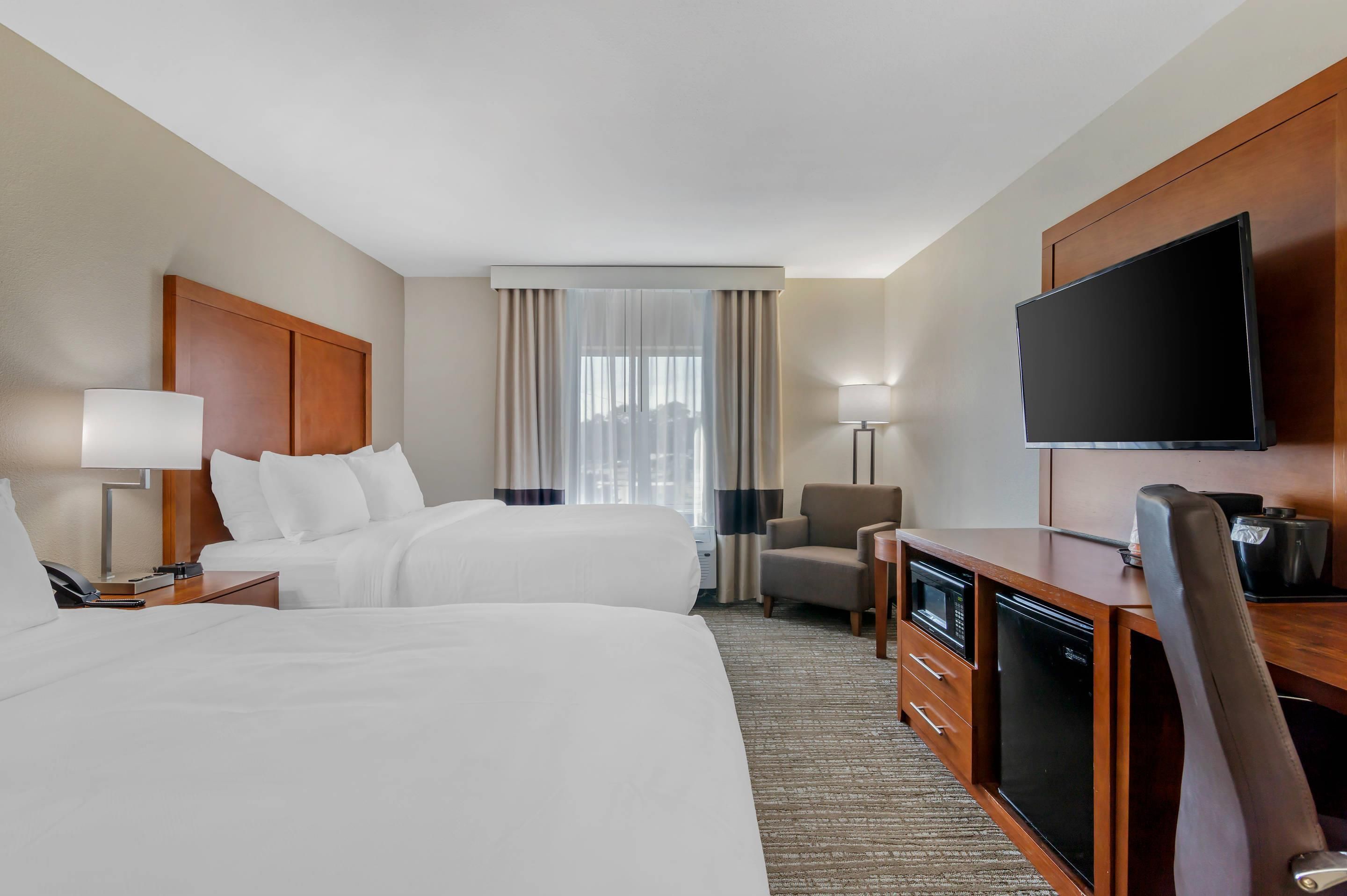 A hotel room with two beds, a desk with a flat-screen TV, a chair, a coffee maker, and a lamp.