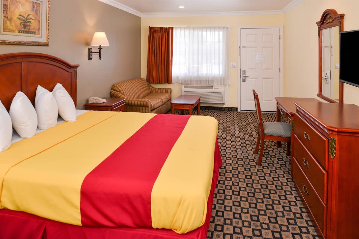 Een hotelkamer met een groot bed, een houten dressoir, een stoel, een bijzettafeltje en een televisie.