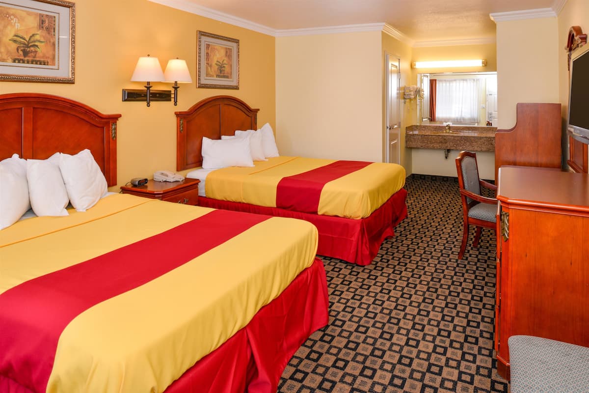 Een hotelkamer met twee bedden, een bureau, een stoel, een spiegel en een badkamer op de achtergrond.
