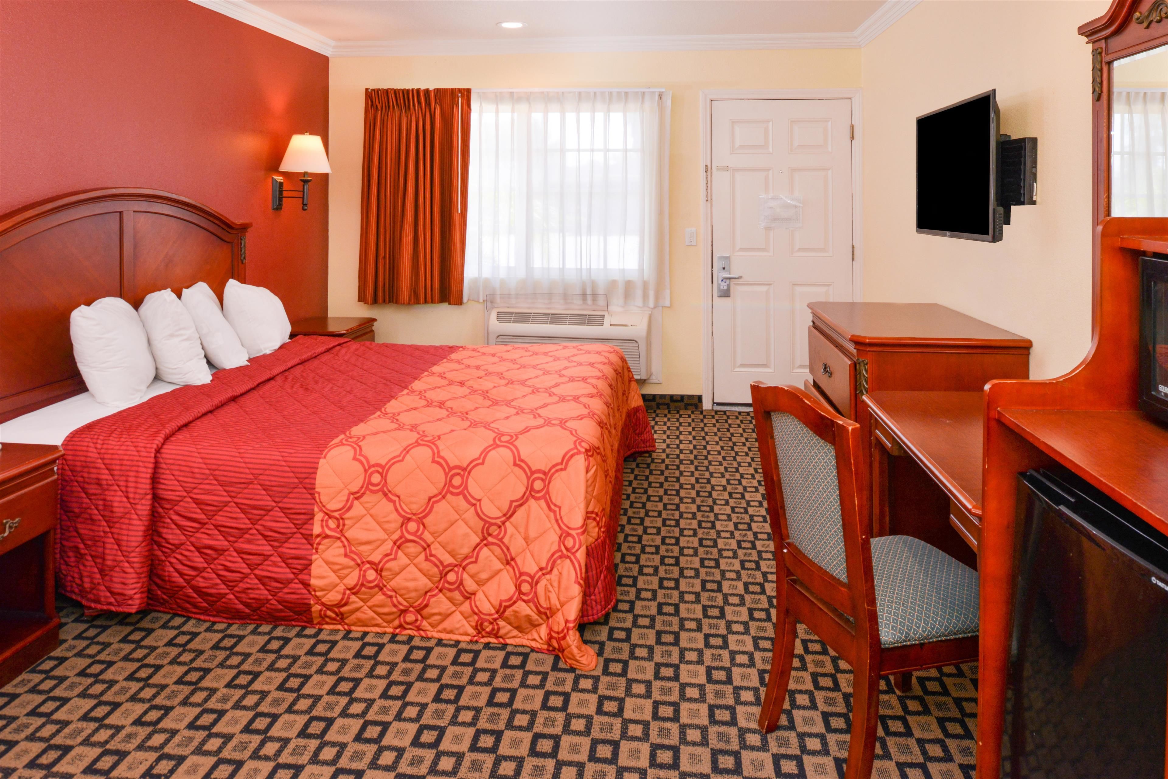 A hotel room with a large bed, a desk, a chair, a television, and a door.