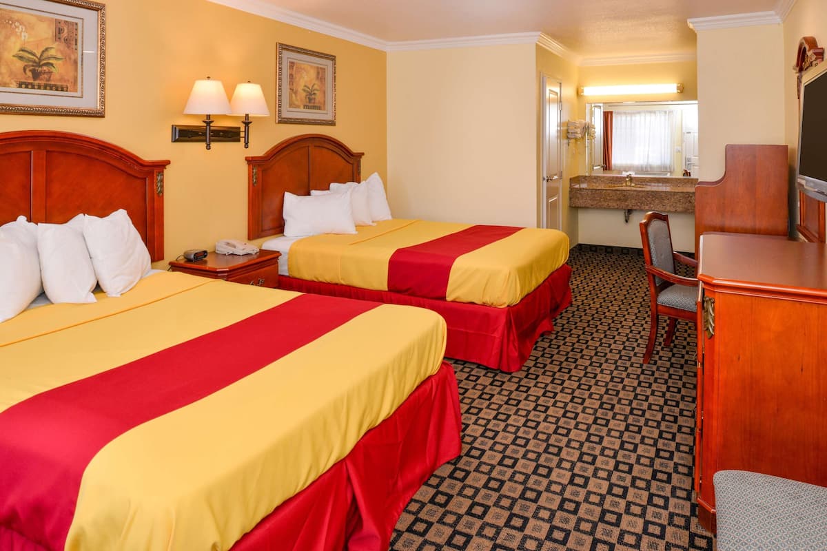 Habitación de hotel con dos camas, un escritorio, una silla, un espejo y un baño a la vista.