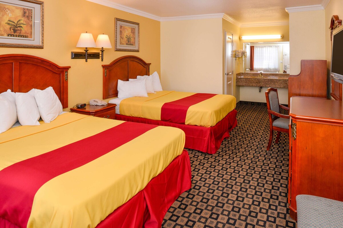 A hotel room with two beds, a desk, a chair, a mirror, and a bathroom visible in the background.